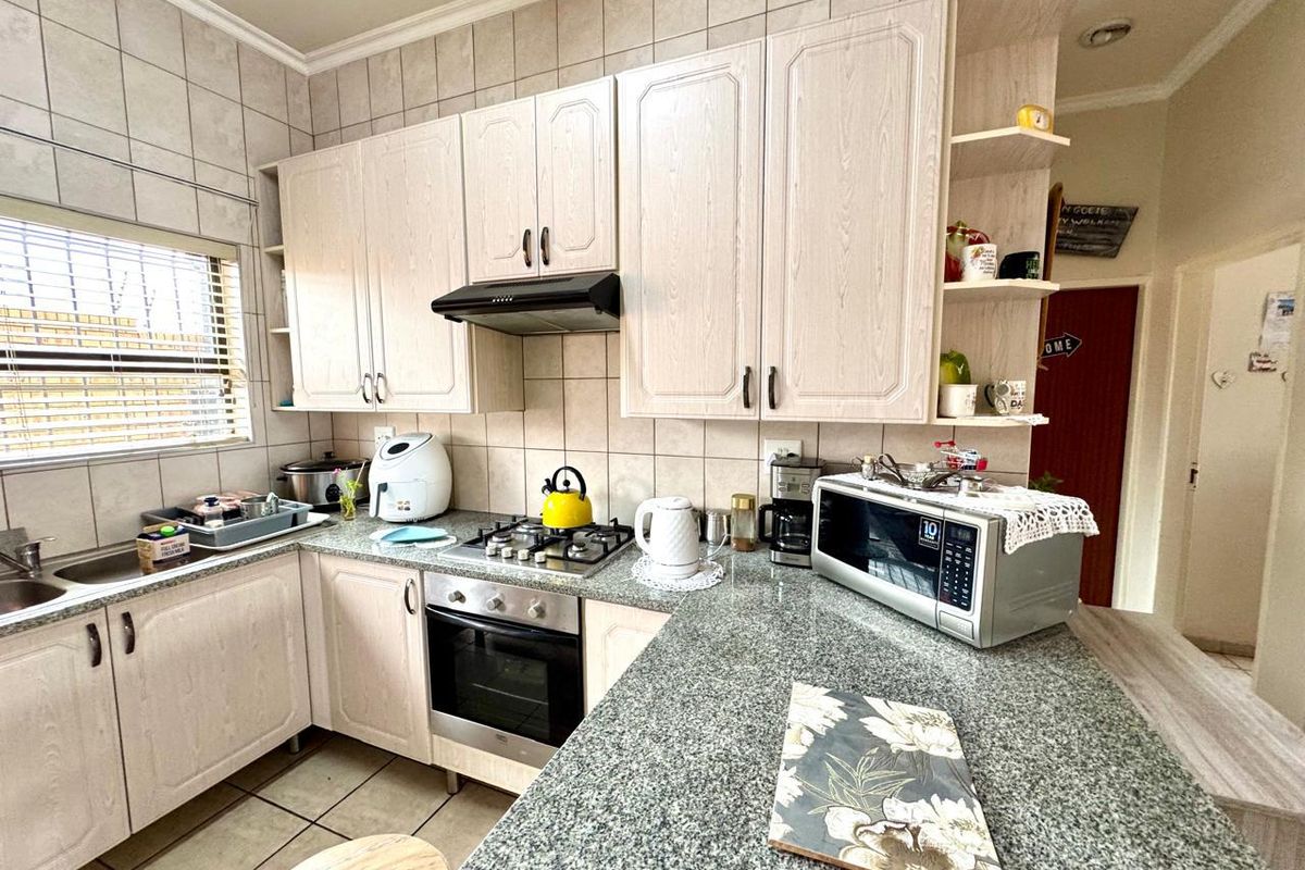 Functional kitchen featuring granite countertops, built-in oven, gas hob, extractor fan, and ample cabinetry with a tiled backsplash and flooring.