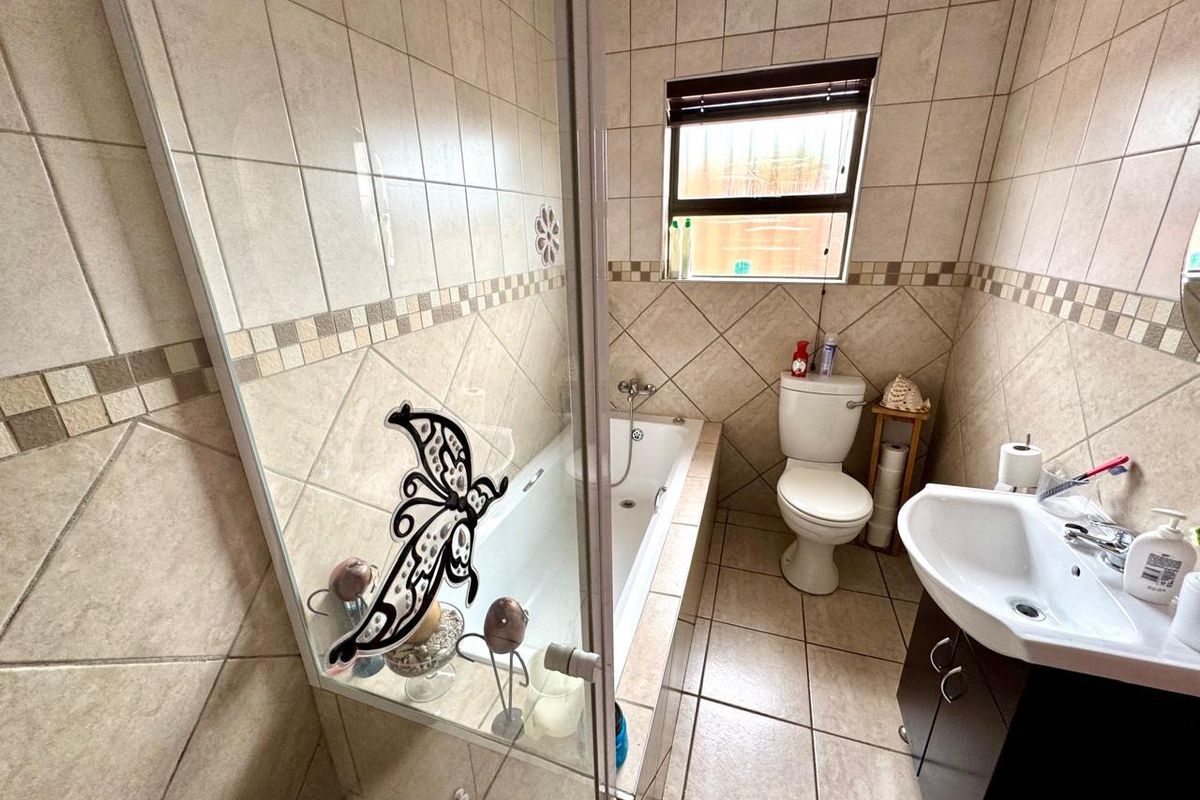 A functional bathroom featuring a built-in bathtub with a glass screen, a toilet, and a vanity basin, finished with neutral ceramic wall and floor tiles.