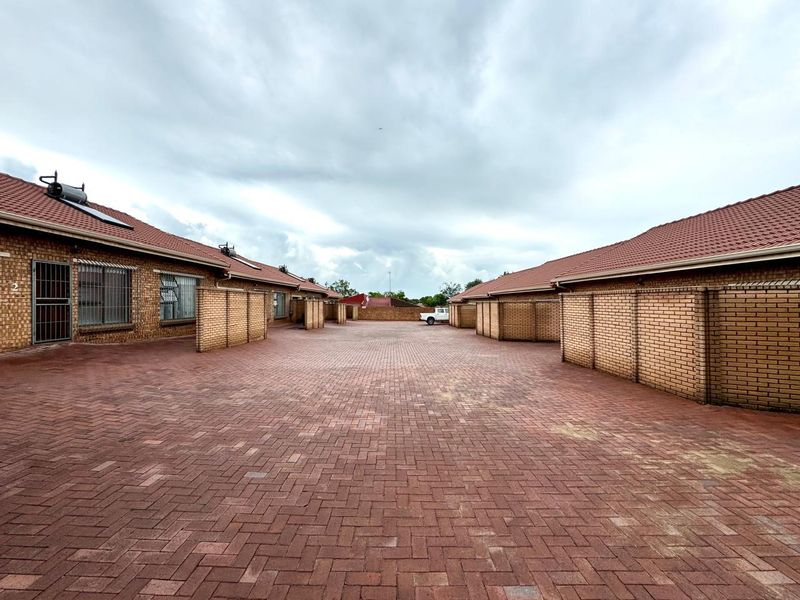 Exterior view of an apartment complex courtyard featuring face brick construction, tiled roofing, and extensive brick paving.