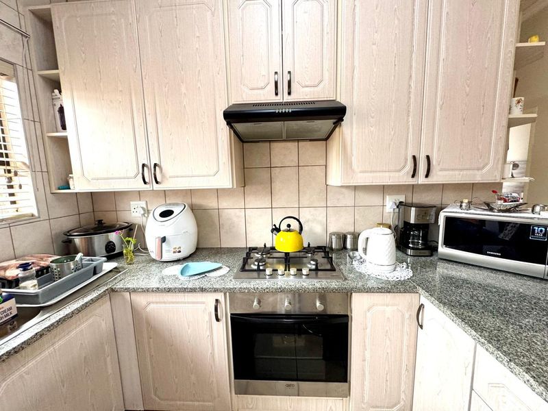 A functional kitchen featuring light wood-grain cabinetry, granite countertops, a gas hob, built-in oven, and a tiled backsplash.