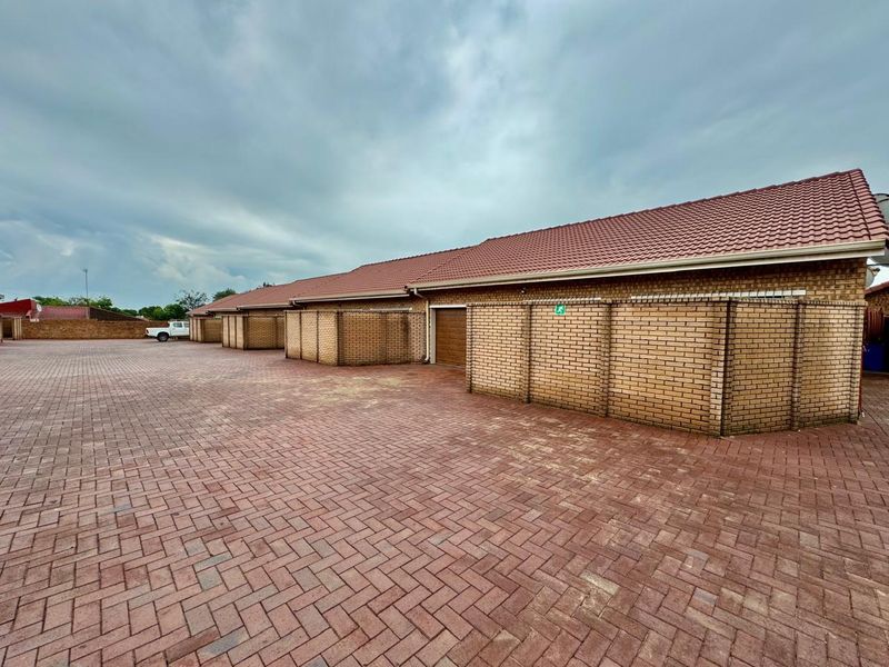 A row of brick-built garages featuring tiled roofing and extensive paved driveway space in a well-maintained residential complex.