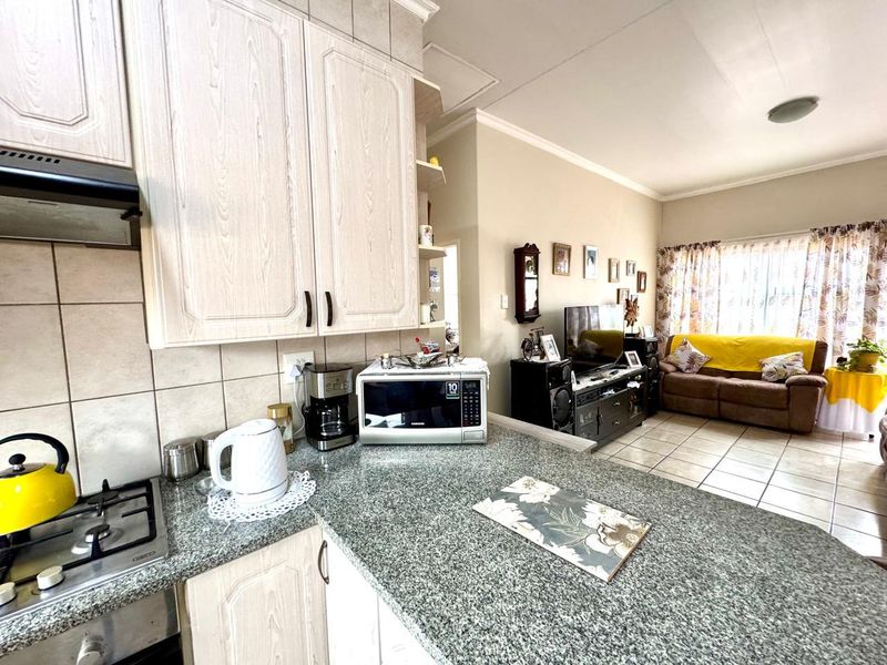 Open-plan living area featuring a kitchen with granite countertops, built-in cabinetry, and a gas hob, flowing into a tiled lounge space.