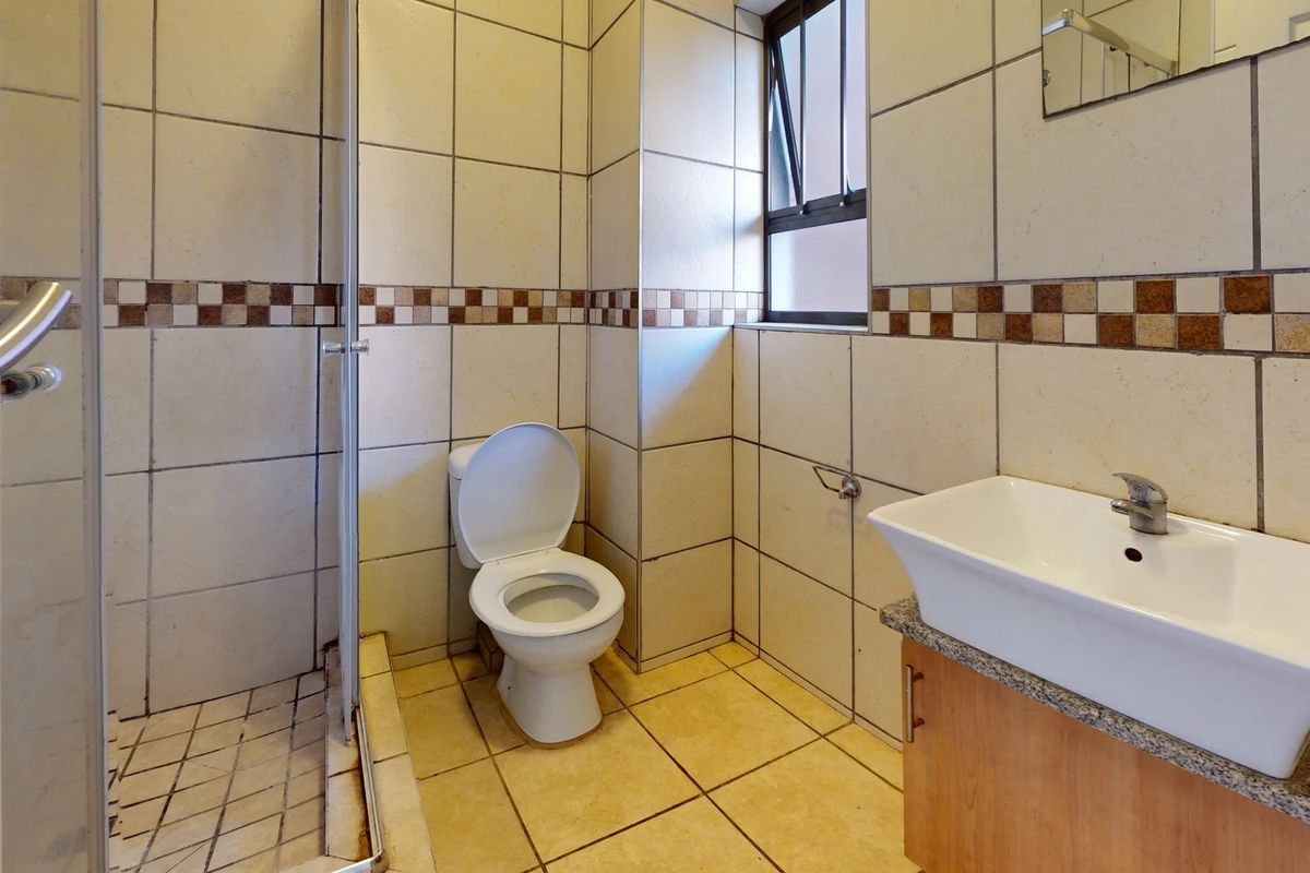 A functional bathroom featuring a shower enclosure, toilet, and vanity basin with tiled finishes throughout.