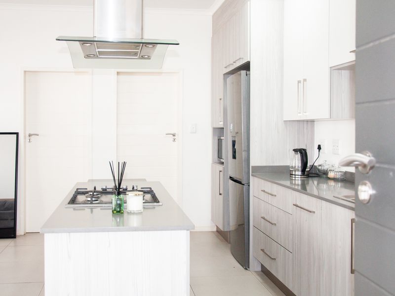 Modern kitchen featuring a central island with a gas hob, extractor fan, stone countertops, and light wood-grain cabinetry.