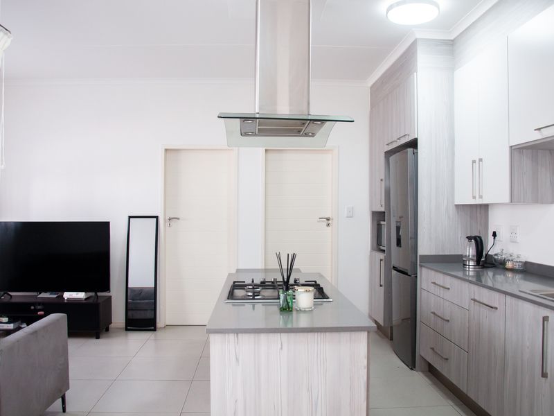 Modern open-plan living area featuring a contemporary kitchen with a central island, gas hob, extractor fan, and sleek cabinetry with stone countertops.