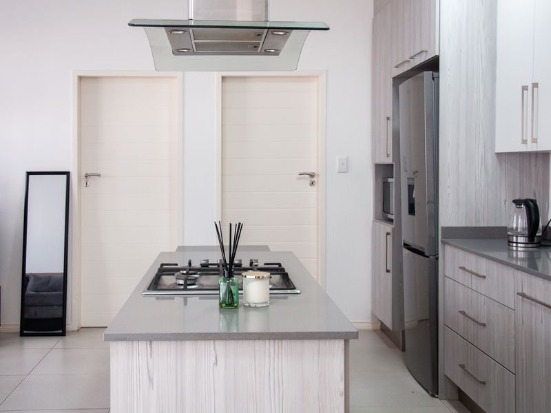 Modern kitchen featuring a central island with a gas hob, overhead extractor fan, stone countertops, and light wood-grain cabinetry.