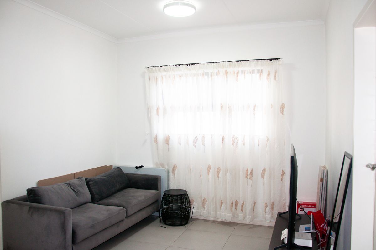A simple living room featuring neutral tiled flooring, white walls, and a window fitted with a curtain rod.