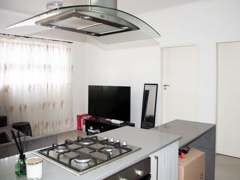 Modern open-plan living area featuring a sleek kitchen island with a gas hob, extractor fan, and built-in oven, seamlessly integrated with the living space.