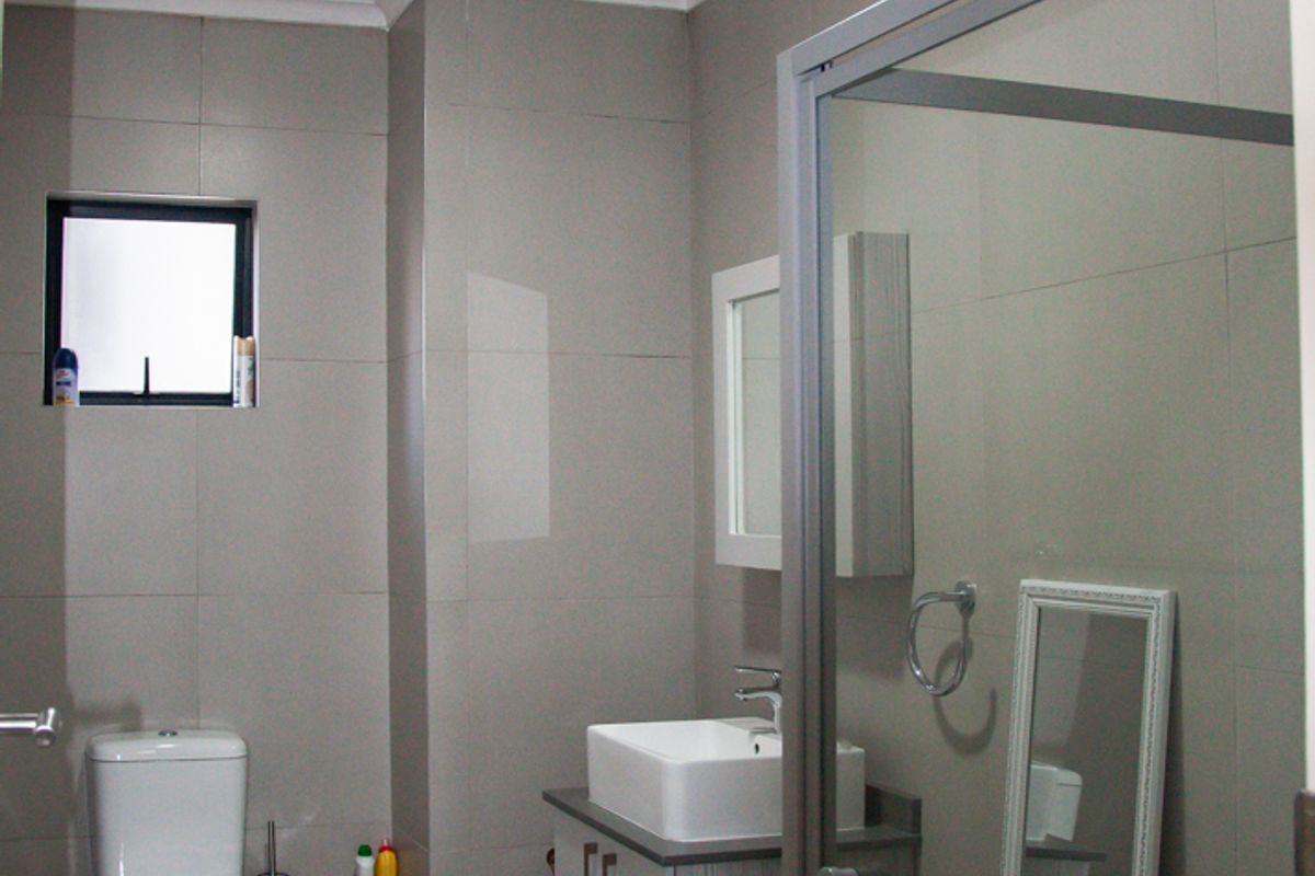 Modern bathroom featuring a wall-mounted vanity with a vessel sink, a glass-enclosed shower, and neutral floor-to-ceiling tiling.