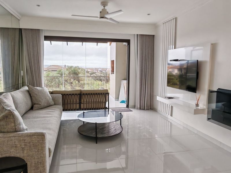 Modern living room featuring polished tile floors, a built-in media console with fireplace, mirrored wall, and large sliding doors leading to a balcony.