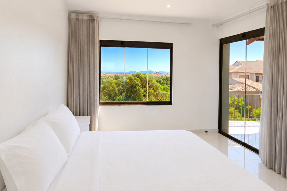 A bright, modern bedroom featuring tiled floors, large sliding glass doors leading to a balcony, and expansive views of the surrounding landscape.