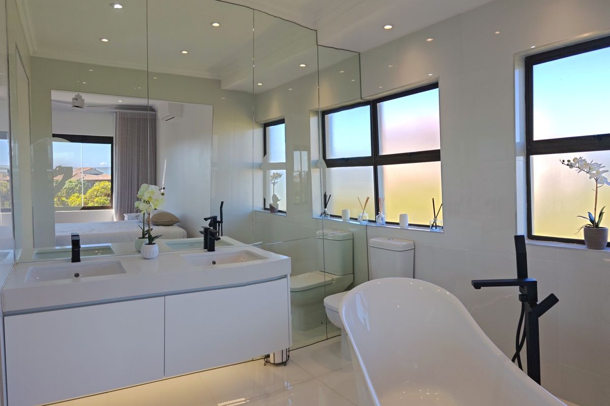 Modern bathroom featuring a double vanity, freestanding bathtub, black fixtures, and extensive wall-to-wall mirrors, creating a bright and contemporary space.