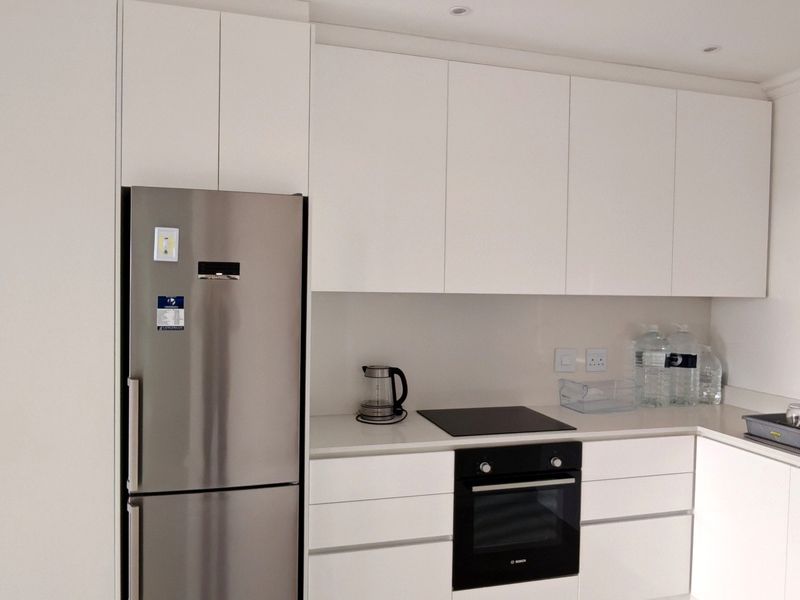 Modern kitchen featuring sleek white cabinetry, stone countertops, integrated appliances, and a stainless steel refrigerator.