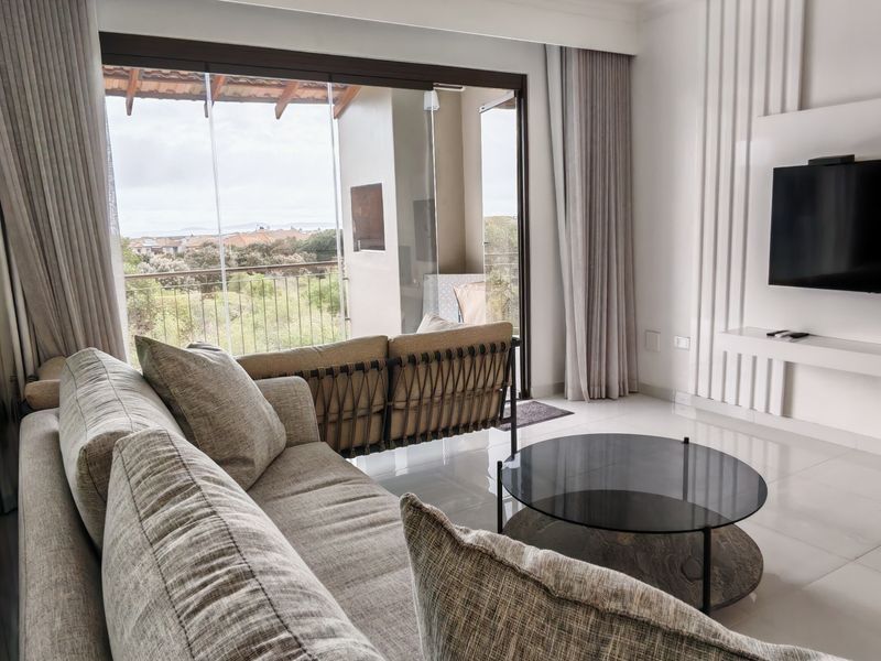 Modern living room featuring a sleek built-in media wall, large format floor tiles, and expansive sliding glass doors leading to a balcony with views.