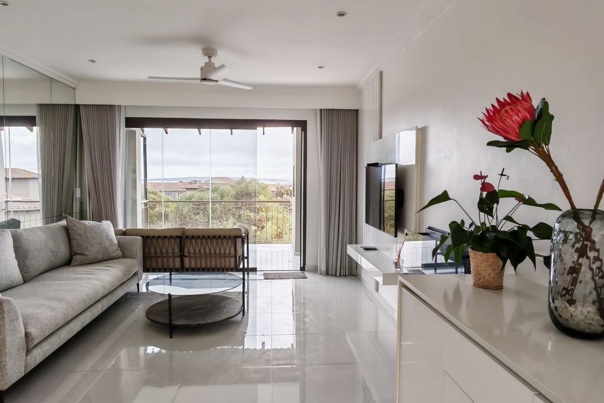 Bright living room featuring a mirrored wall, tiled flooring, ceiling fan, and sliding glass doors leading to an outdoor balcony area.