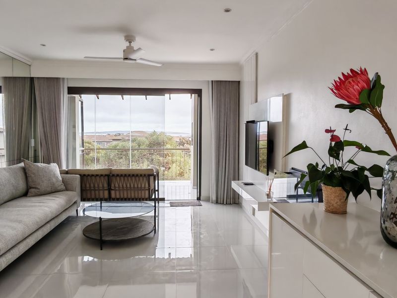 Bright living room featuring a mirrored wall, tiled flooring, ceiling fan, and sliding glass doors leading to an outdoor balcony area.