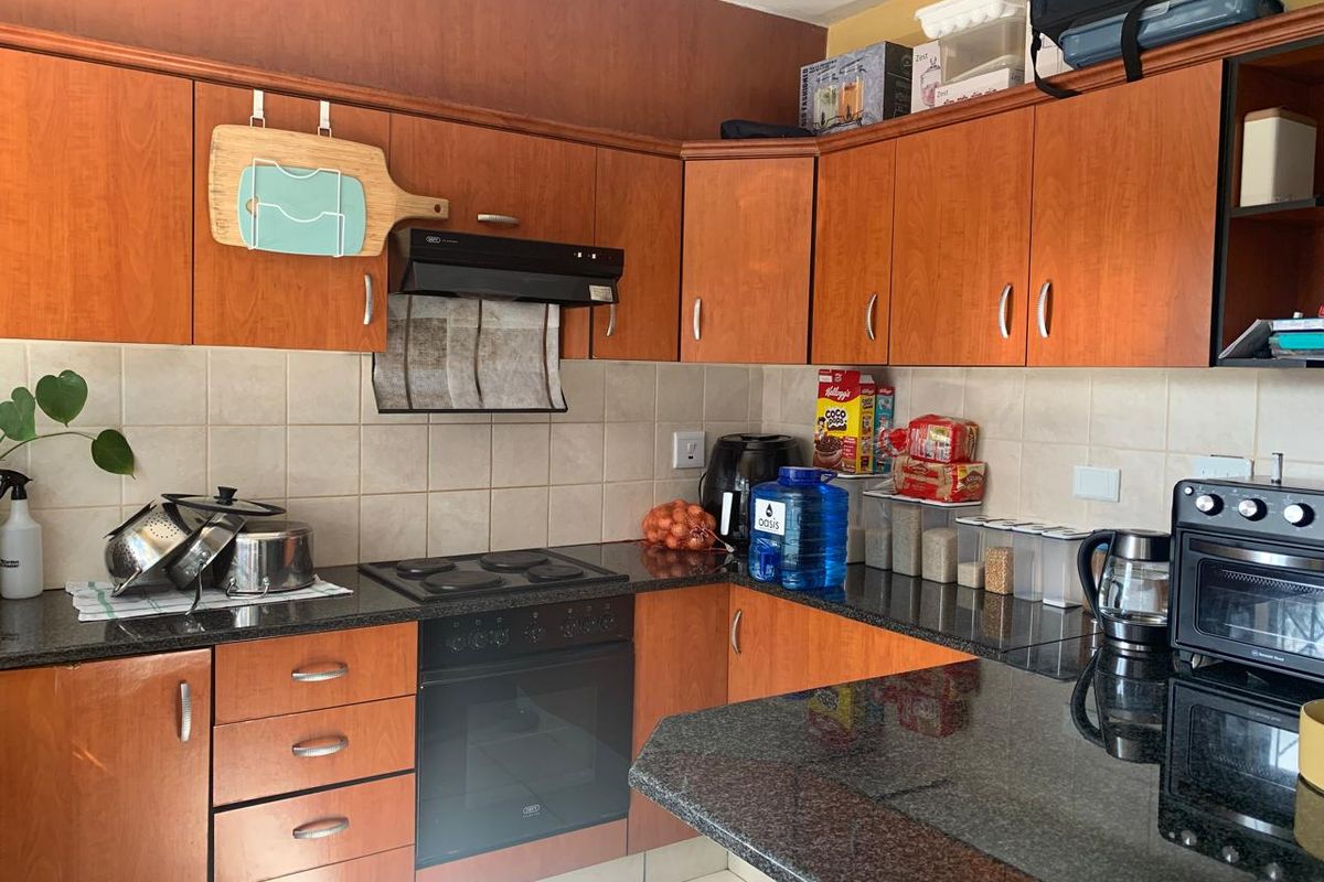 A functional kitchen featuring wood-finish cabinetry, granite countertops, a built-in oven, and an electric hob with a tiled backsplash.