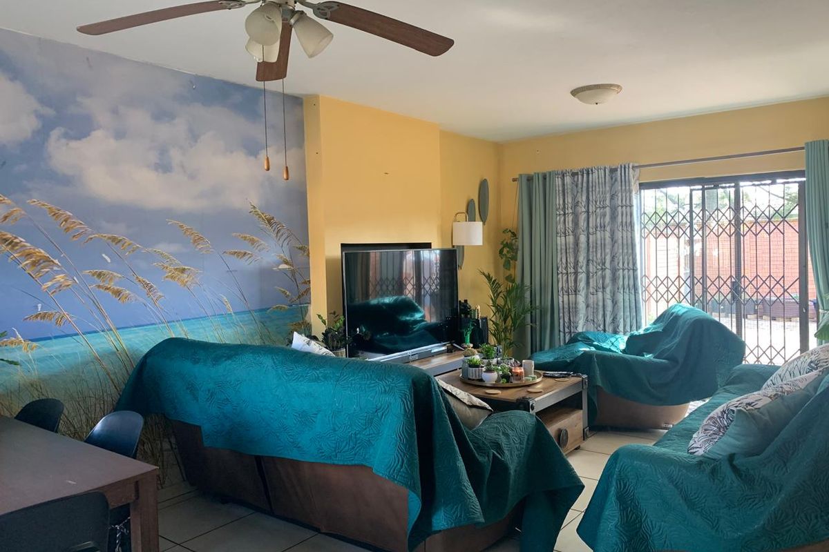 A living room featuring tiled flooring, a ceiling fan, and sliding glass doors with security gates leading to the exterior.