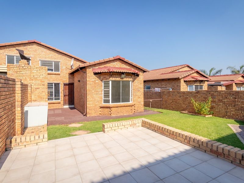 Rear view of a face brick townhouse featuring a paved patio area, private garden, and secure boundary walls.