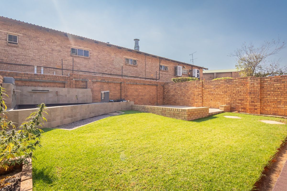 Private rear garden featuring a brick boundary wall, raised brick planter, lawn area, and a built-in water feature.