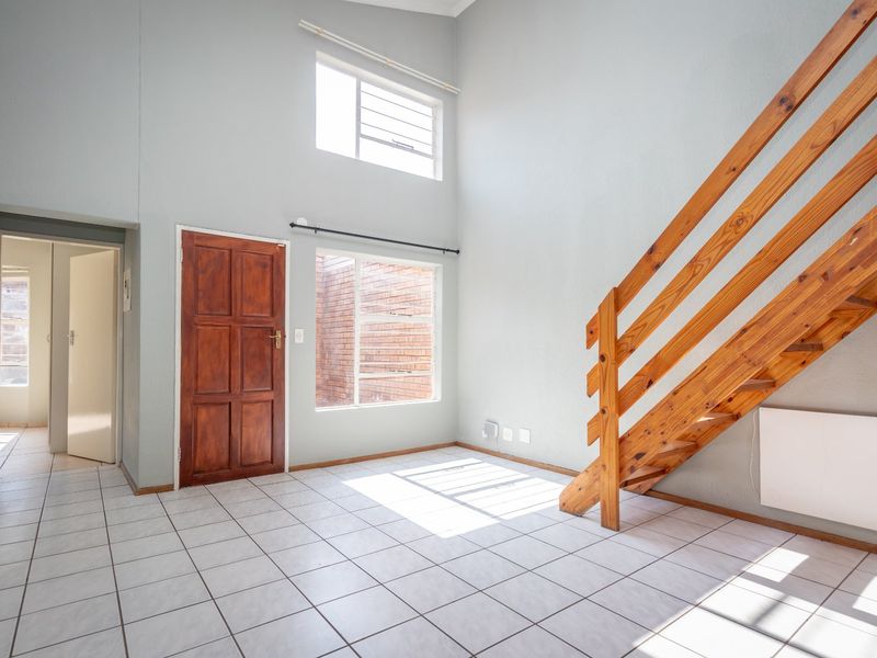 Bright, double-volume living area featuring tiled flooring, a wooden staircase, and natural light from large windows, offering a clean, blank canvas for interior design.