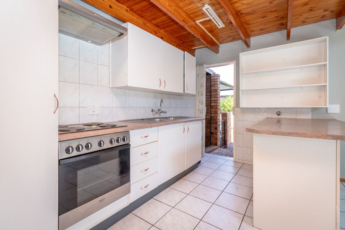 Functional kitchen featuring white cabinetry, laminate countertops, built-in oven with hob, tiled flooring, and exposed timber ceiling beams with direct access to the exterior.
