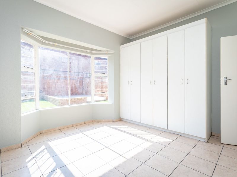 Bright and spacious bedroom featuring large bay windows, neutral tiled flooring, and extensive built-in cupboard storage.