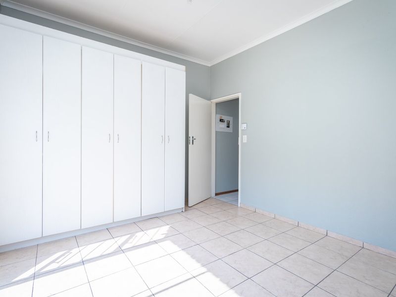 A bright, empty bedroom featuring neutral wall paint, tiled flooring, and extensive built-in cupboard storage.