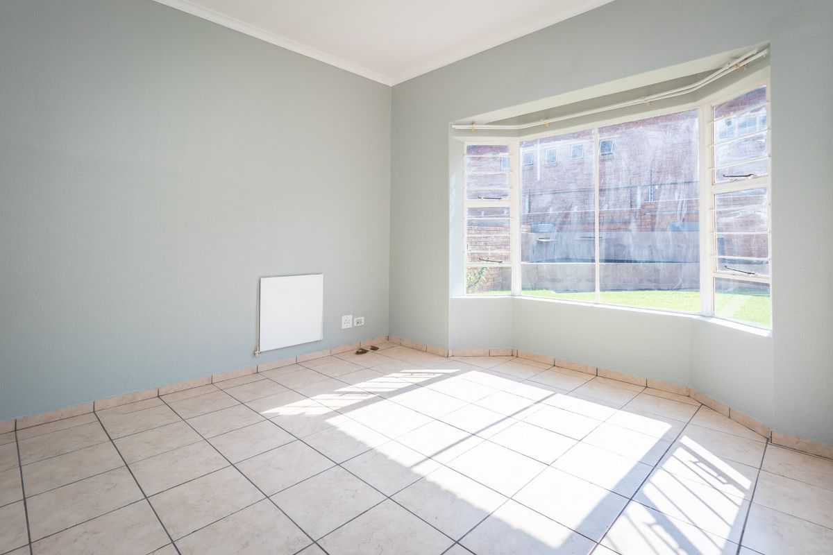A bright, empty bedroom featuring tiled flooring, a large bay window, and a wall-mounted heater, offering a clean canvas for personalization.