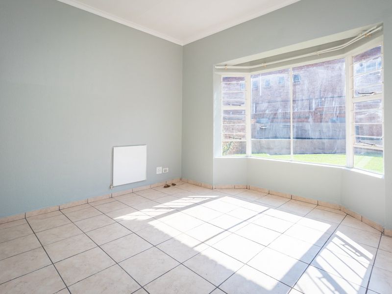 A bright, empty bedroom featuring tiled flooring, a large bay window, and a wall-mounted heater, offering a clean canvas for personalization.