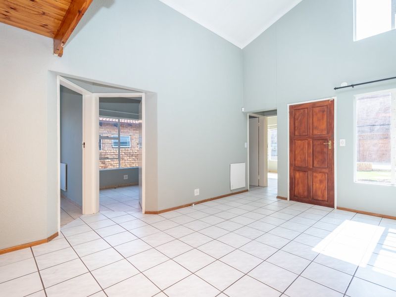 Spacious living area featuring vaulted ceilings with exposed timber beams, ceramic tiled flooring, and natural light through large windows.