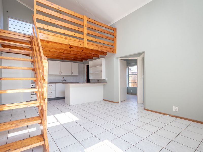 Open-plan living area featuring a wooden mezzanine level, staircase, and a functional kitchen with breakfast counter and tiled flooring throughout.