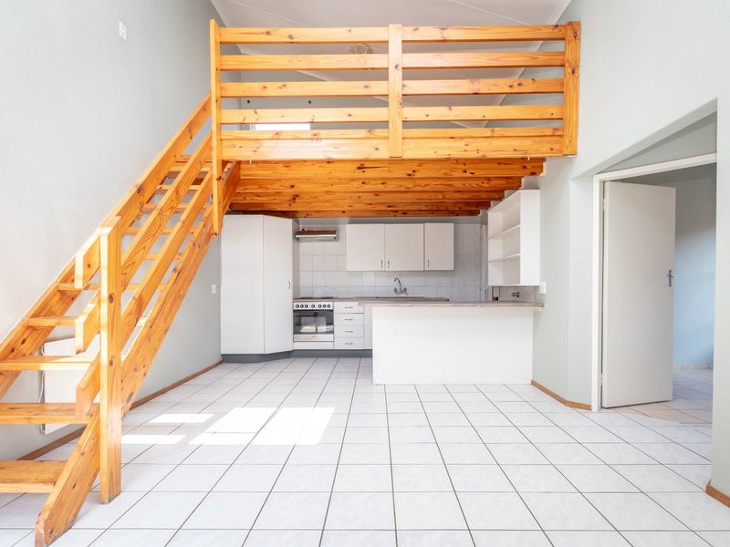 Open-plan living area featuring a wooden mezzanine level, staircase, and a functional kitchen with built-in cabinetry and tiled flooring.