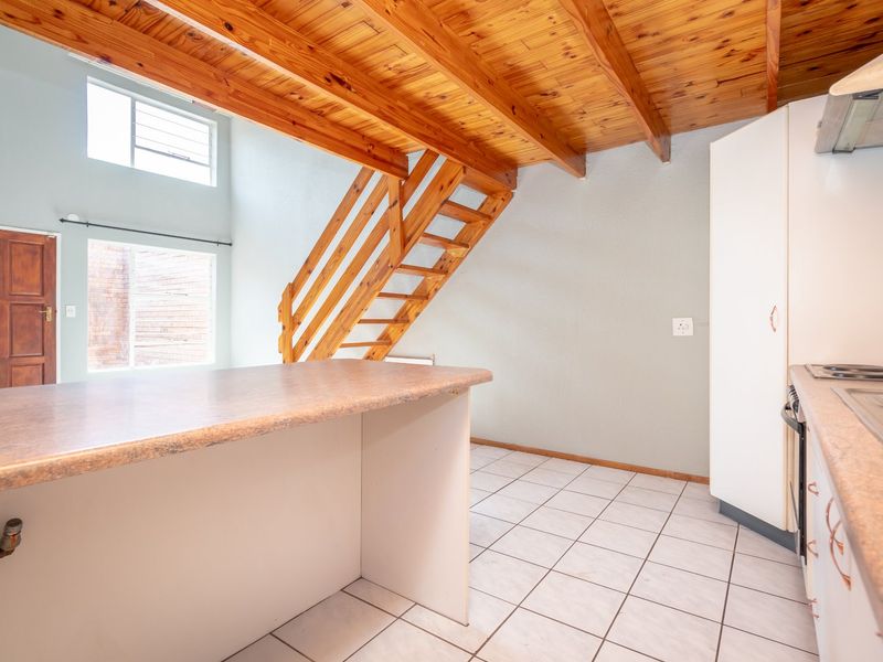 Open plan kitchen and living area featuring a timber staircase, exposed wooden ceiling beams, tiled flooring, and built-in cabinetry with a breakfast bar.