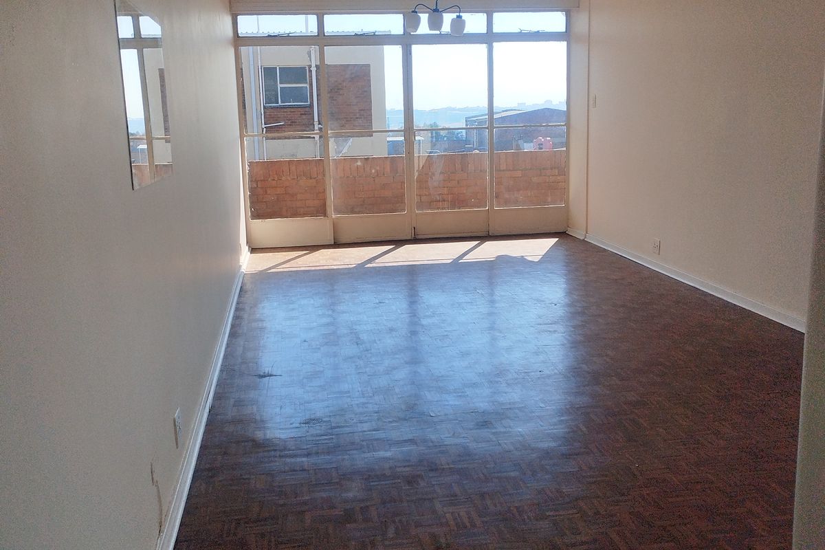 An empty living room featuring original parquet flooring, large glass sliding doors leading to a balcony, and neutral wall finishes.
