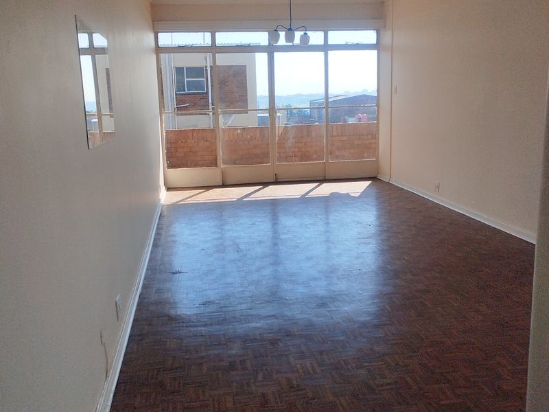 An empty living room featuring original parquet flooring, large glass sliding doors leading to a balcony, and neutral wall finishes.