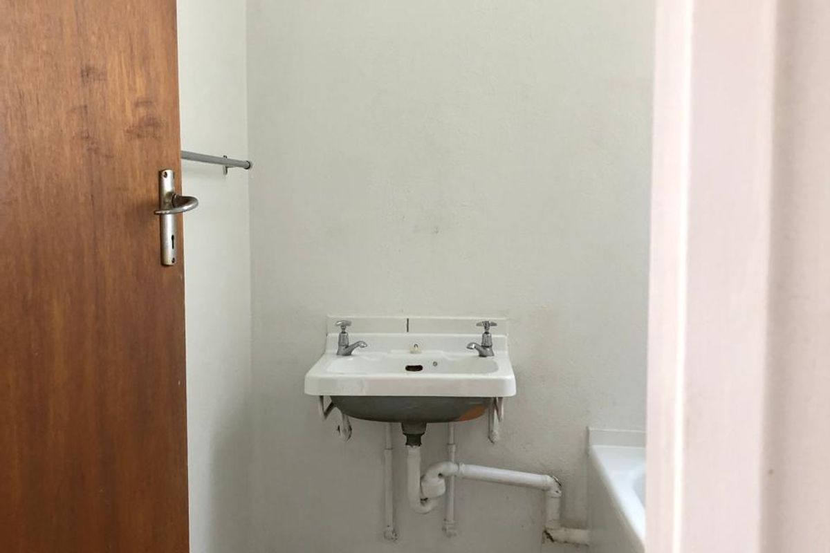 A compact, dated bathroom featuring a wall-mounted basin with exposed plumbing and tiled flooring, offering potential for a modern renovation.