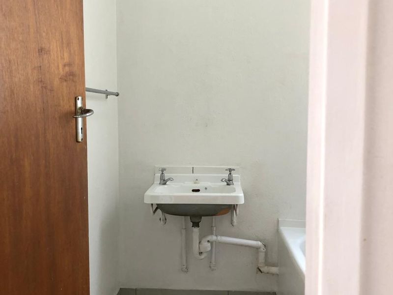 A compact, dated bathroom featuring a wall-mounted basin with exposed plumbing and tiled flooring, offering potential for a modern renovation.