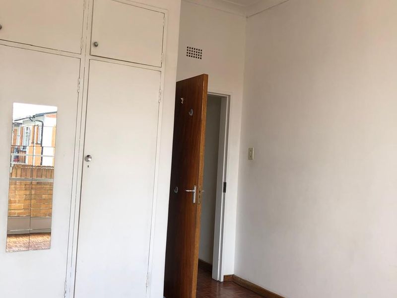 A bright, empty bedroom featuring classic parquet flooring, built-in storage cupboards, and a neutral color palette, ready for personalization.