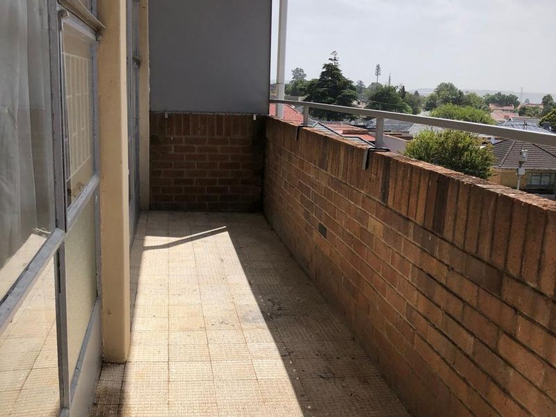 An open-air balcony featuring a brick balustrade, metal railing, and tiled flooring, offering an elevated view of the surrounding neighborhood.