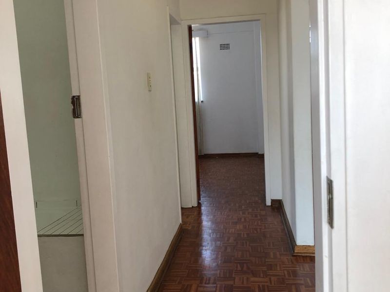 A clean, empty hallway featuring traditional parquet flooring and white walls, providing access to multiple rooms within the apartment.
