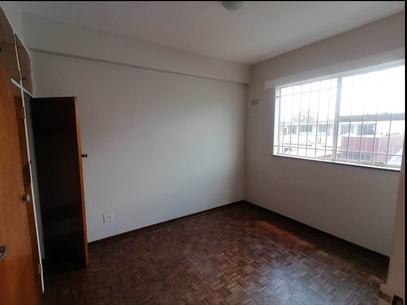 A vacant bedroom featuring classic parquet flooring, a built-in wooden cupboard, and a window fitted with security bars.