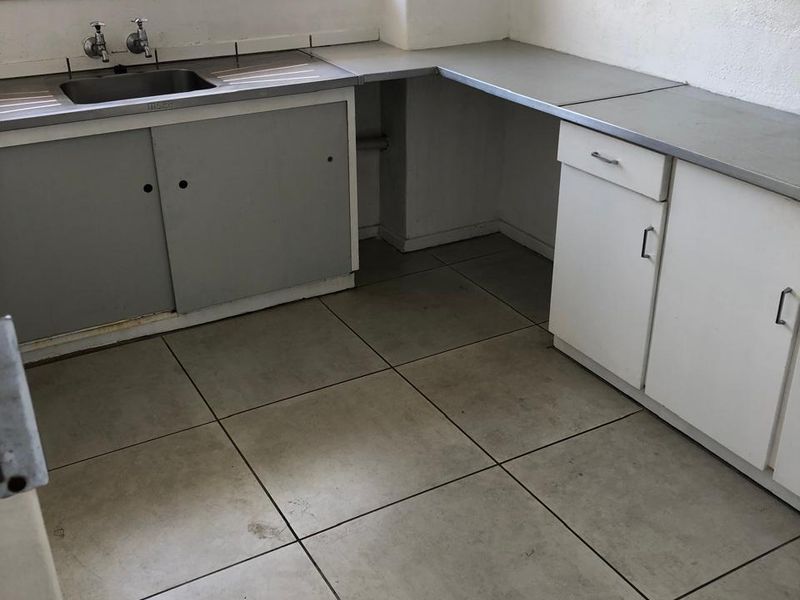 A functional kitchen space featuring built-in cabinetry, a stainless steel sink, and tiled flooring, ready for renovation or modernization.