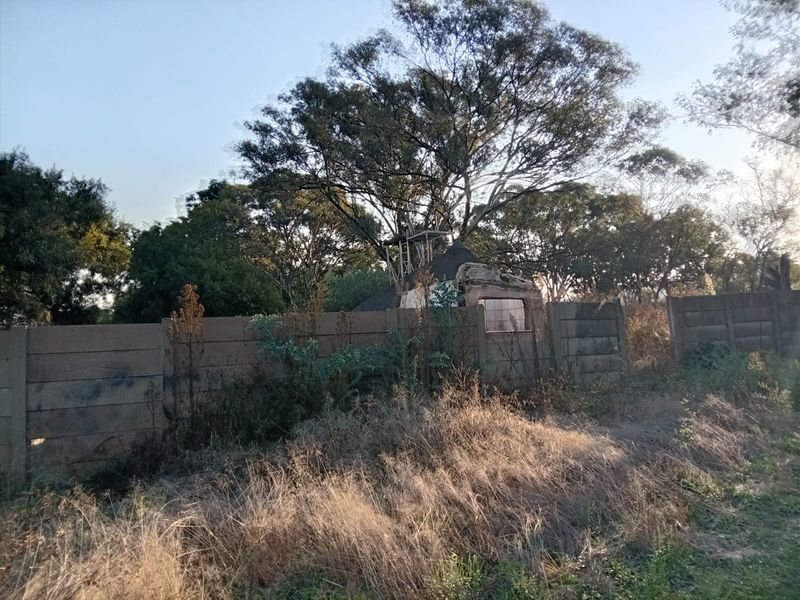 View of a vacant residential plot featuring an overgrown landscape, a dilapidated boundary wall, and remnants of a small structure.