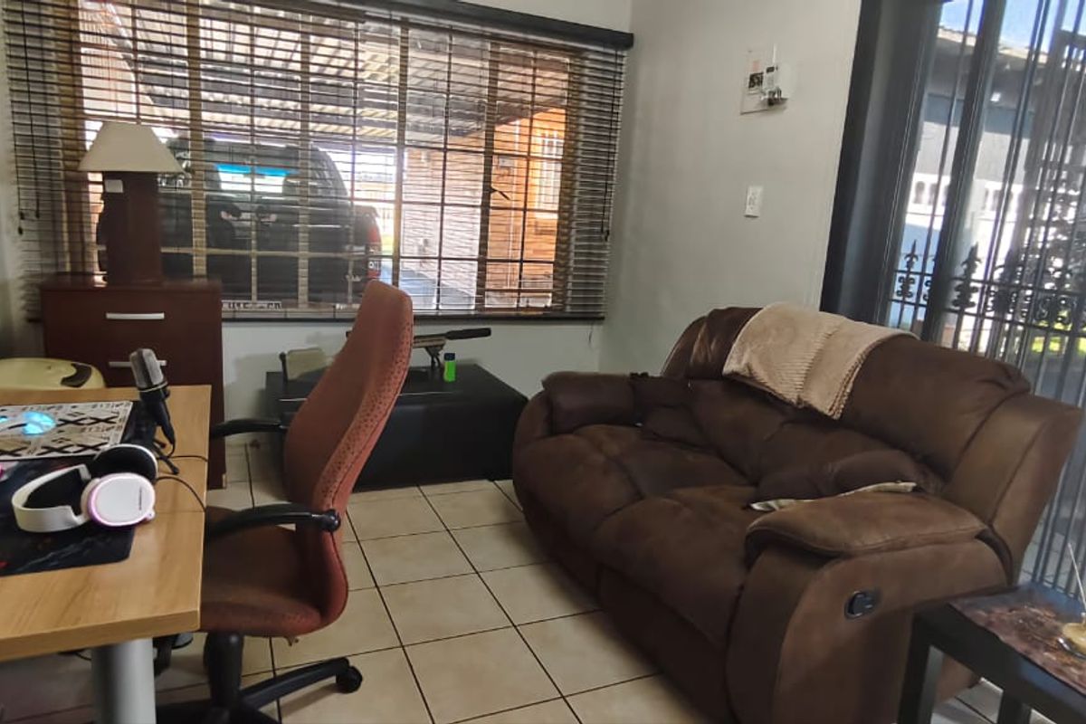 A multi-purpose living area featuring tiled flooring, large windows with blinds, and direct access to an outdoor patio space.