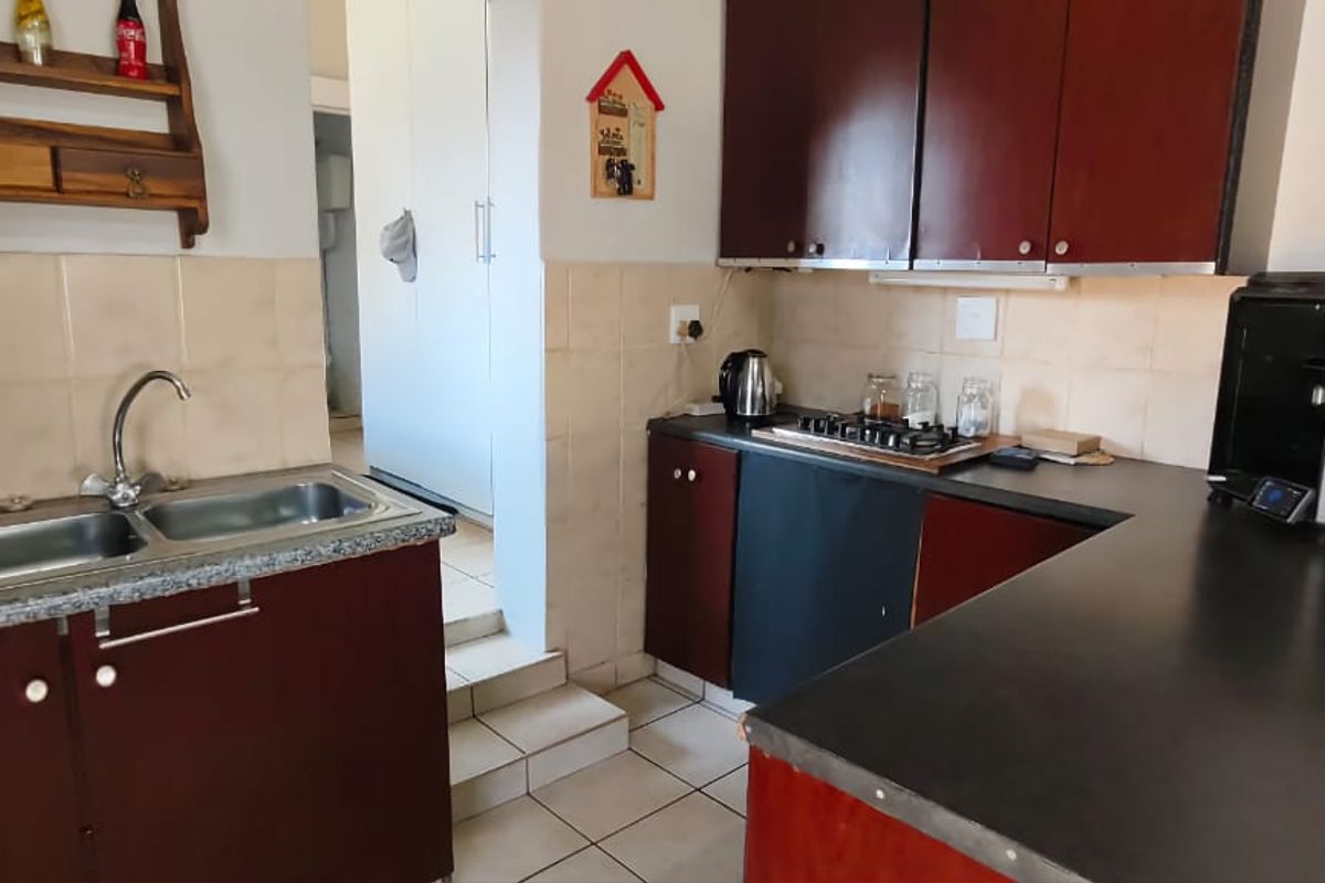 A functional kitchen featuring dark wood-finish cabinetry, a double stainless steel sink, and tiled flooring with a step leading to an adjacent area.