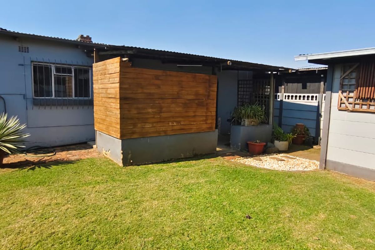 A view of the rear exterior area featuring a lawn, a wooden privacy screen, and adjacent outbuilding structures.