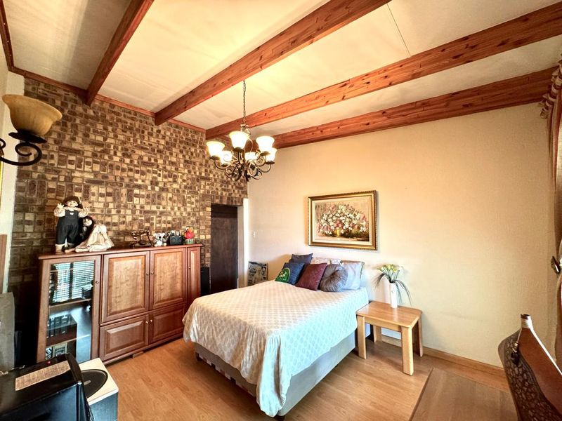 A bedroom featuring exposed timber ceiling beams, a textured brick feature wall, and laminate flooring, offering a rustic aesthetic.
