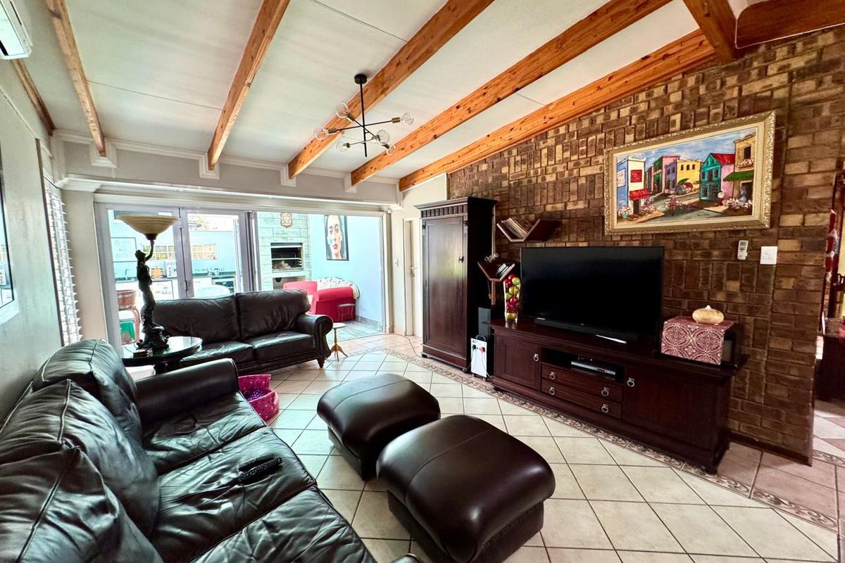 Spacious living room featuring exposed timber ceiling beams, a rustic brick feature wall, tiled flooring, and large sliding doors opening to an outdoor patio area.