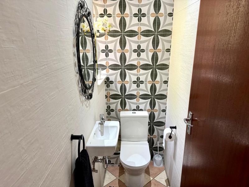 A compact guest bathroom featuring a modern wall-mounted basin, toilet, and decorative patterned feature wall tiles.